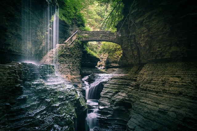 Waterfalls, layered rock, and a stone bridge framed by a green gorge