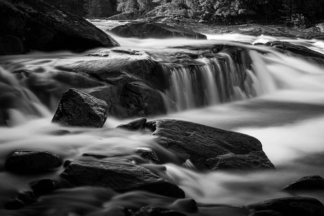 Long-exposure water flowing over dark woodland rocks