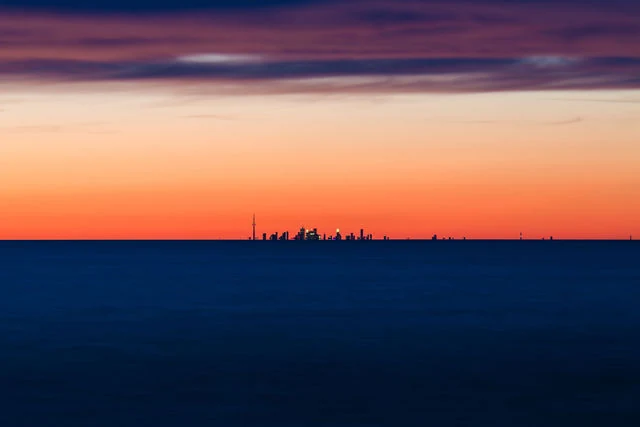 A distant skyline beneath orange and violet sky across blue water