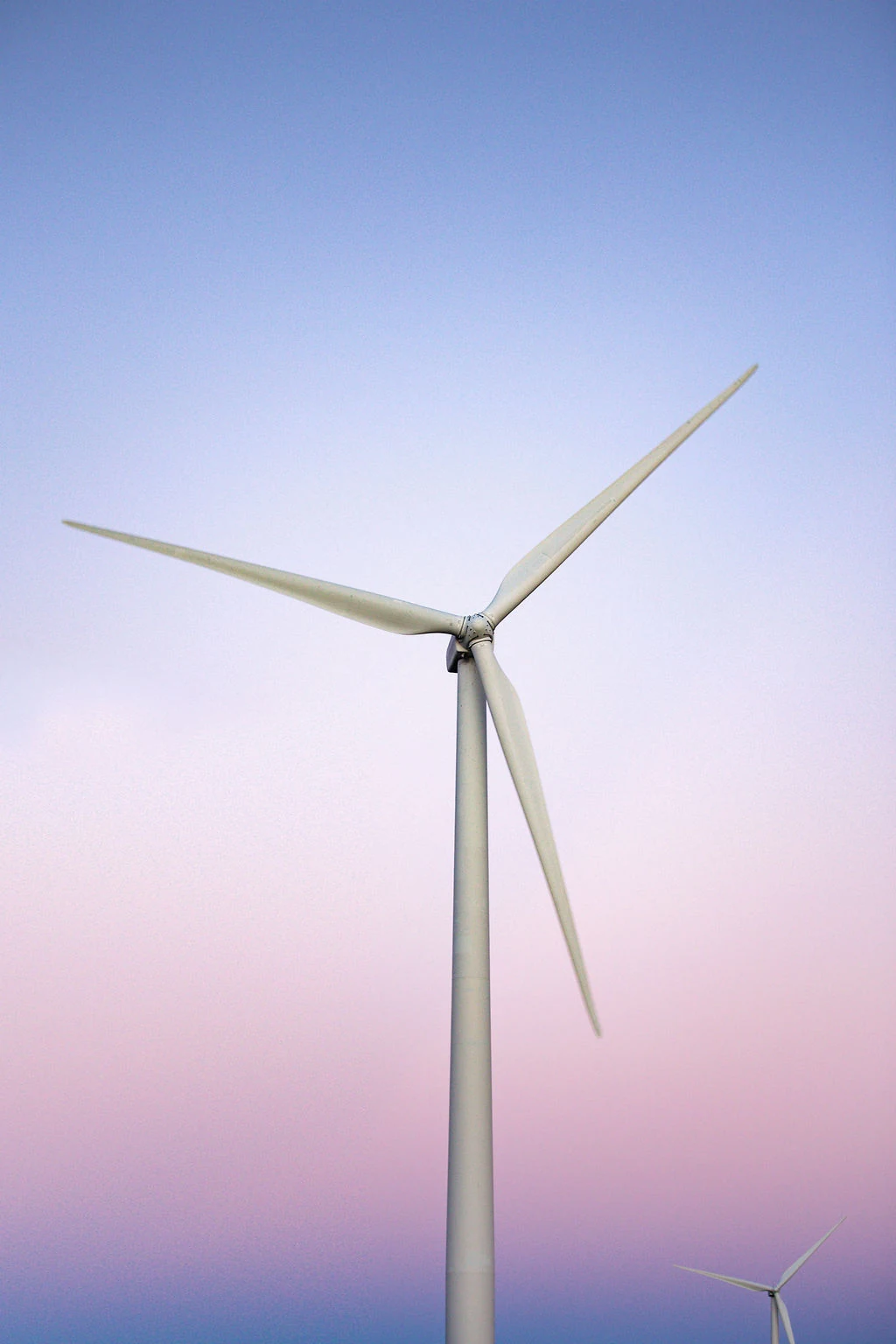 A white wind turbine against a soft violet and pink evening sky